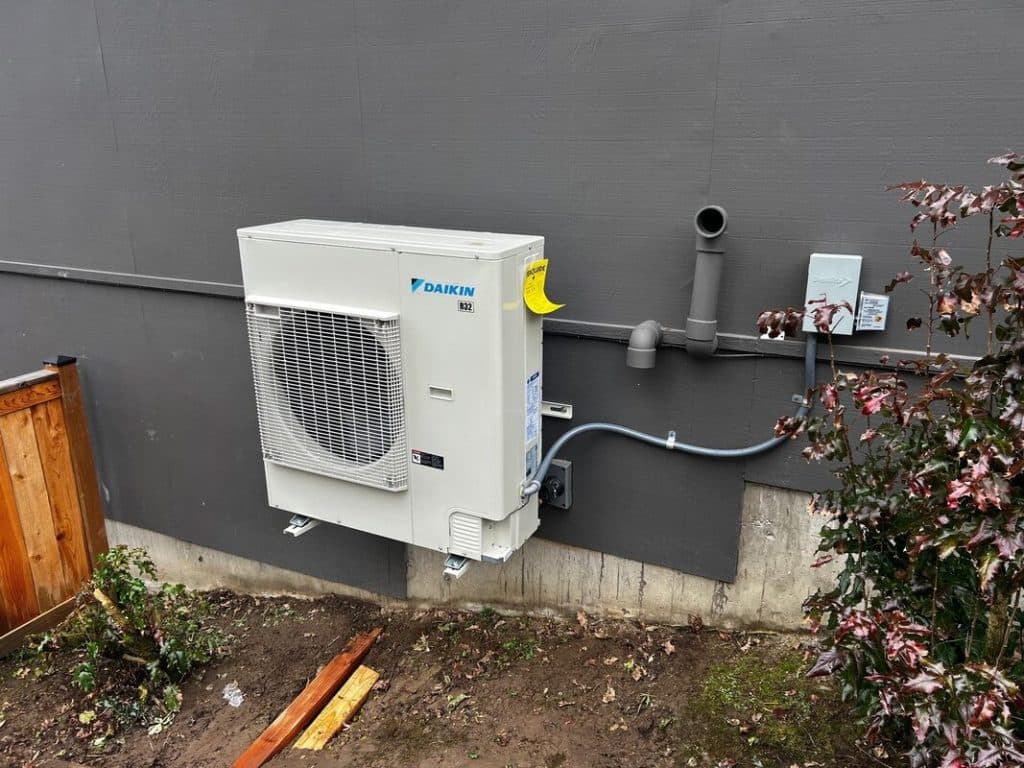 A wall-mounted indoor unit connected to copper and insulated lines, the install clean and squared to the wall.