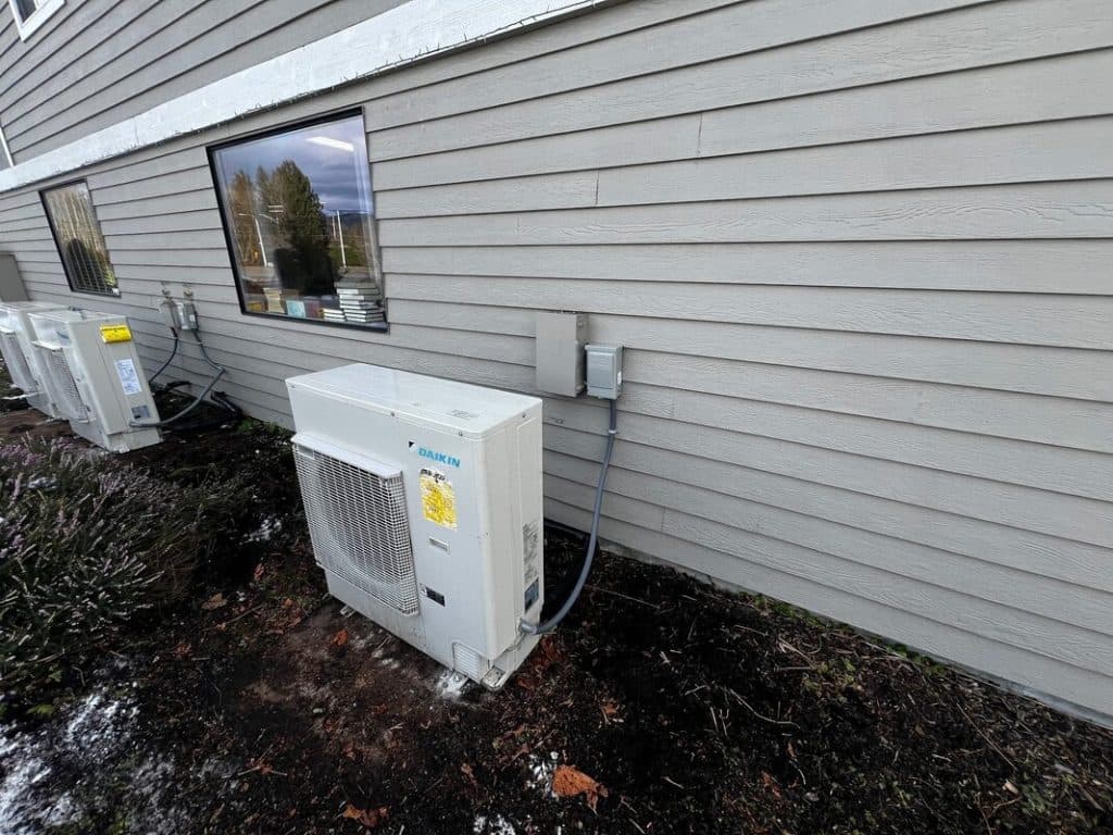 A Daikin heat pump condenser installed on its pad beside a home, the unit that delivers both heating and cooling.