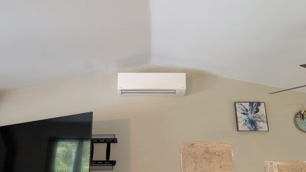 A white ductless mini-split head mounted high on an interior wall below a vaulted ceiling.