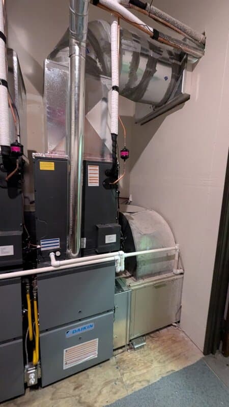 An indoor air handler and connected equipment in a utility space, galvanized duct and insulated lines run to the unit.