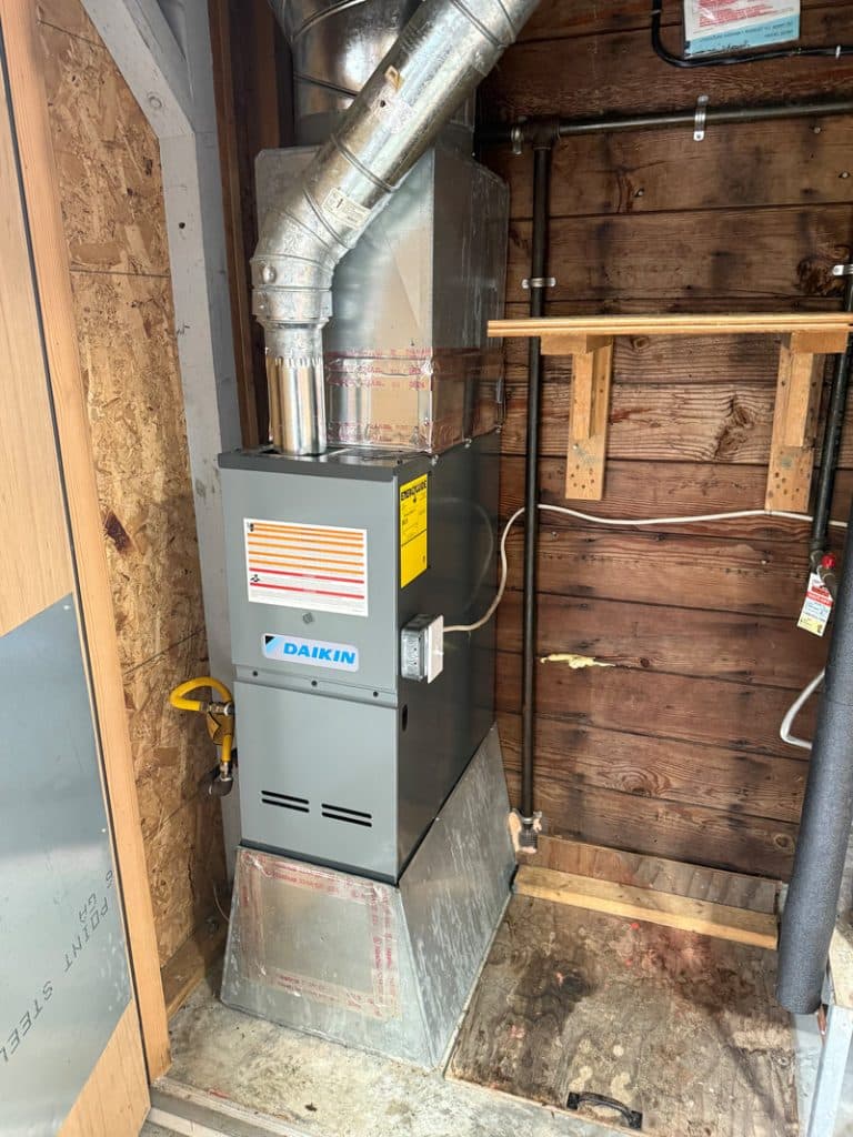 A Daikin gas furnace and connected ductwork installed in a utility closet, the flue and supply plenum run overhead.